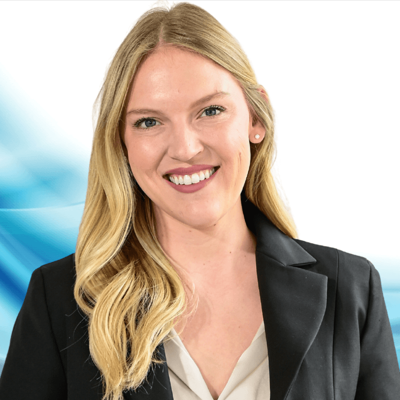 Smiling professional woman with blonde hair in a black blazer, light beige blouse, against a blue abstract background.