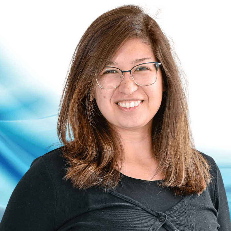 Smiling woman with glasses in a black top, leaning slightly to the side, against a blue abstract background.