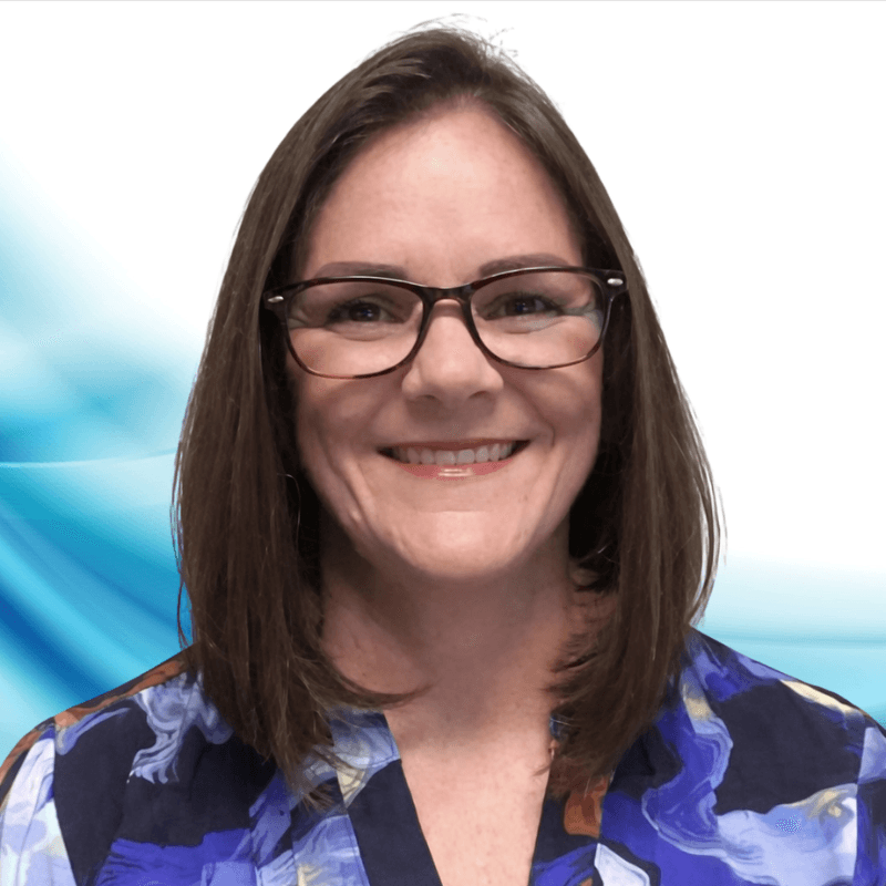 Portrait of a smiling woman with shoulder-length brown hair and glasses, wearing a blue patterned blouse, against a light blue abstract background.