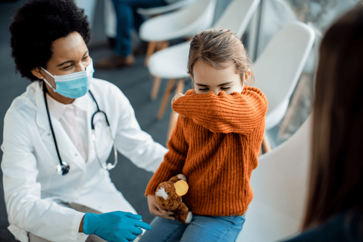 doctor shows young girl how to cough into elbow to prevent spread of virus