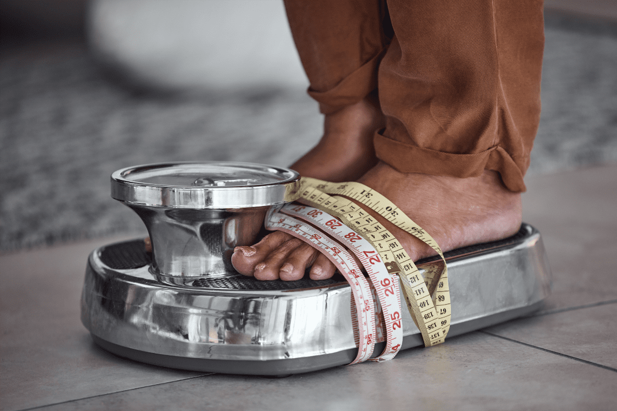 person on scale with measuring tape to symbolize eating disorder