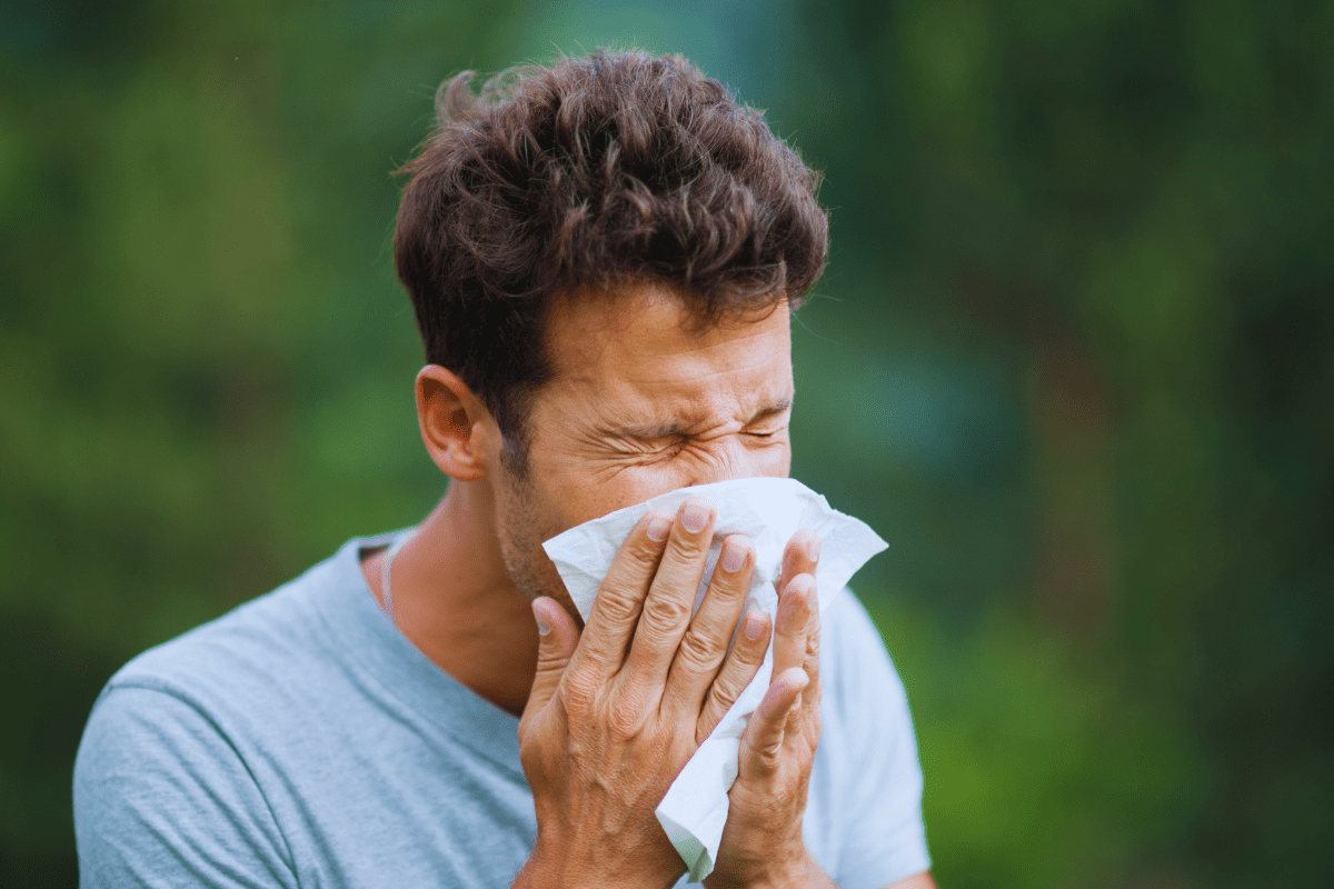 man blowing his nose with either allergies or a cold
